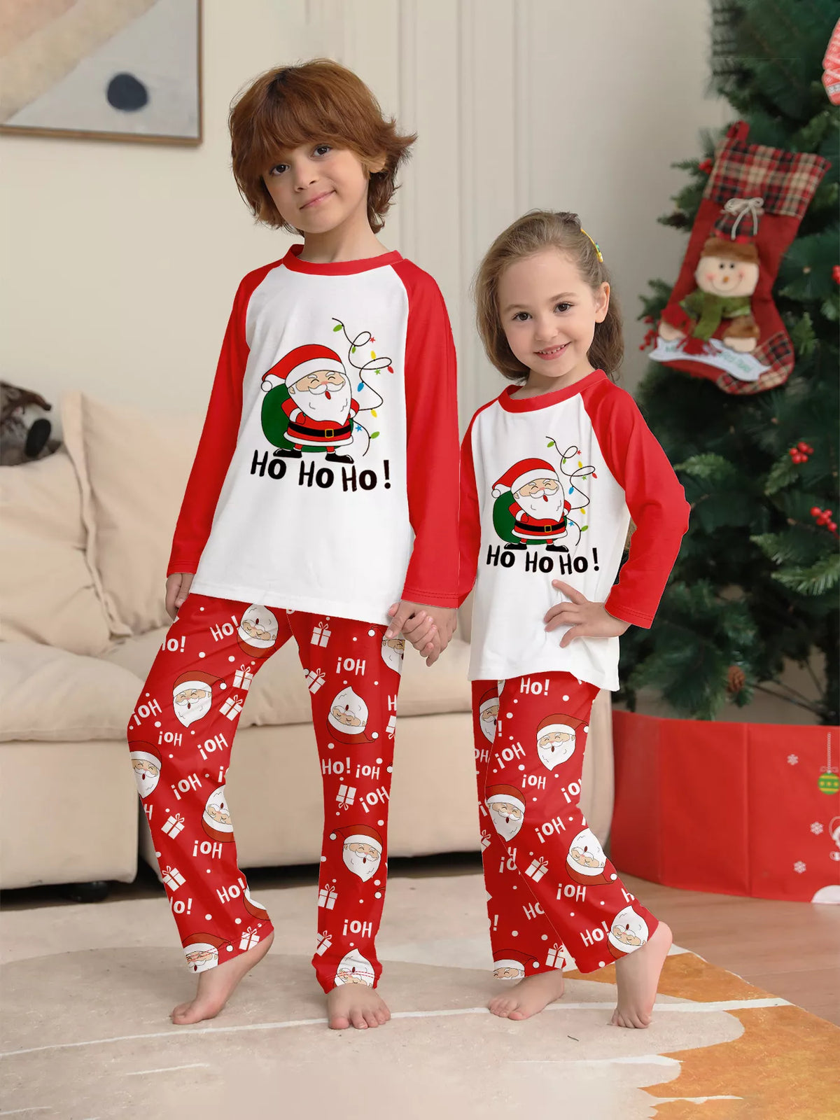 Two children wearing matching white Santa tops with red sleeves and printed red pants.