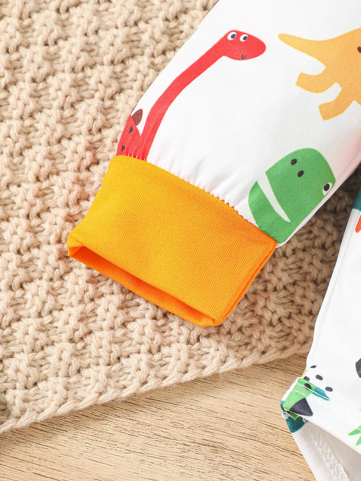 Orange cuff and dinosaur-print sleeve detail on the baby bodysuit