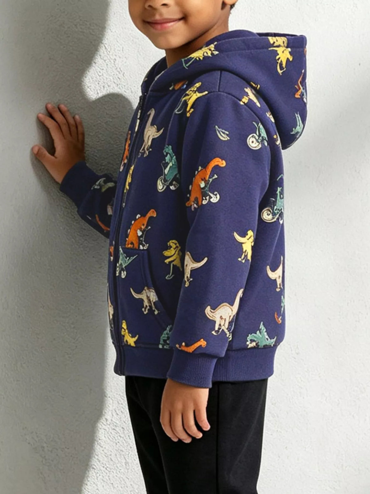 Side view of a child wearing the navy dinosaur-print hooded jacket.