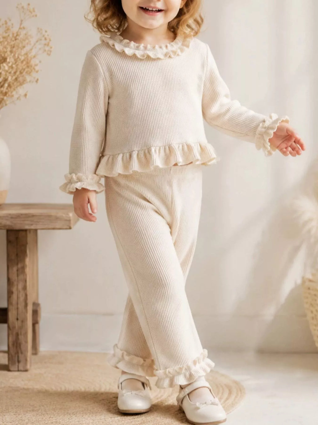 Child wearing a cream long-sleeve ruffle-trim top and matching pants.