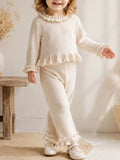 Child wearing a cream long-sleeve ruffle-trim top and matching pants.