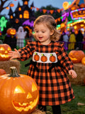 Children’s orange and black plaid smocked dress with pumpkin embroidery worn by a child
