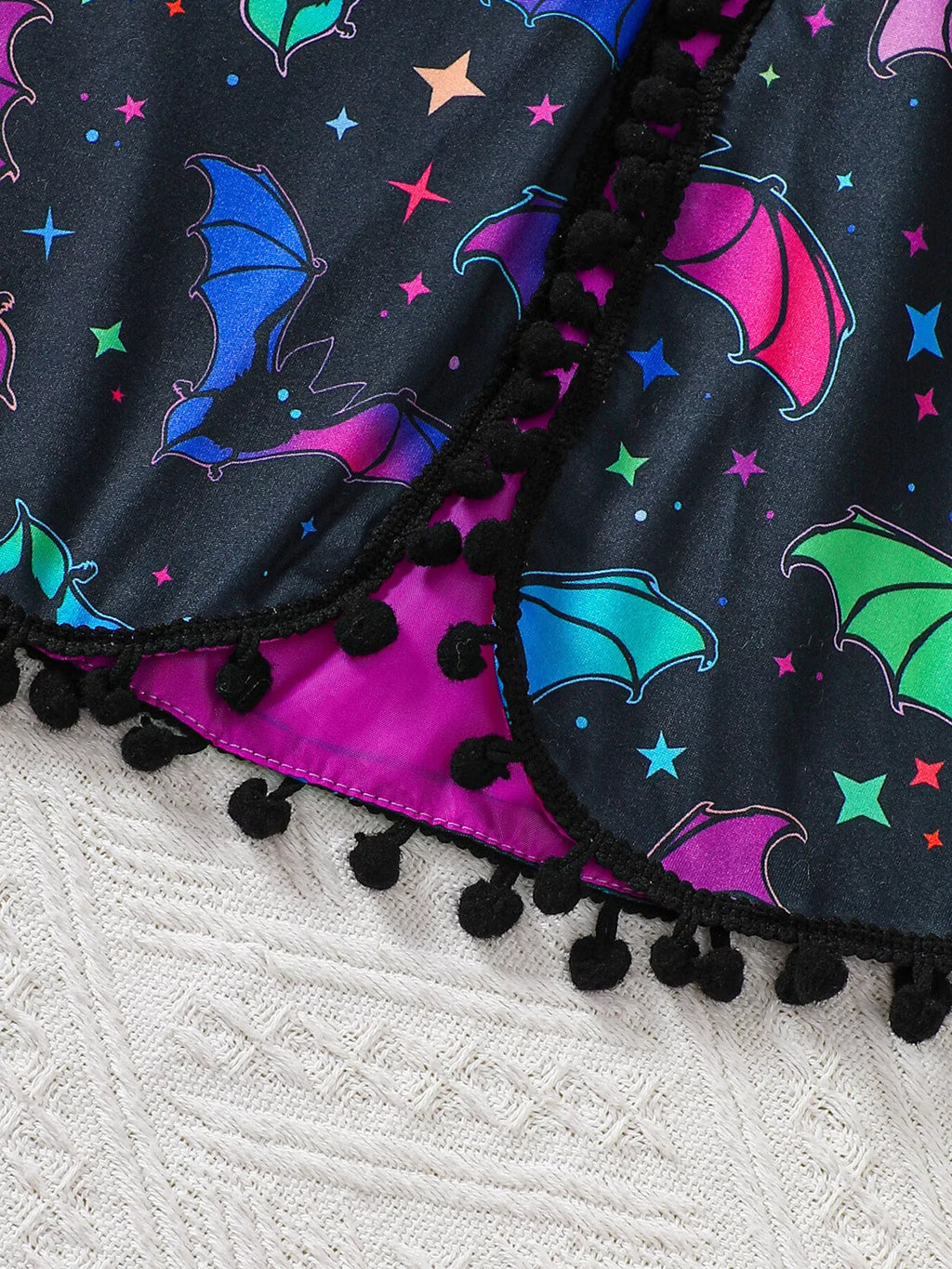 Close-up of colorful bats, stars and black pom-pom edging on the cape.