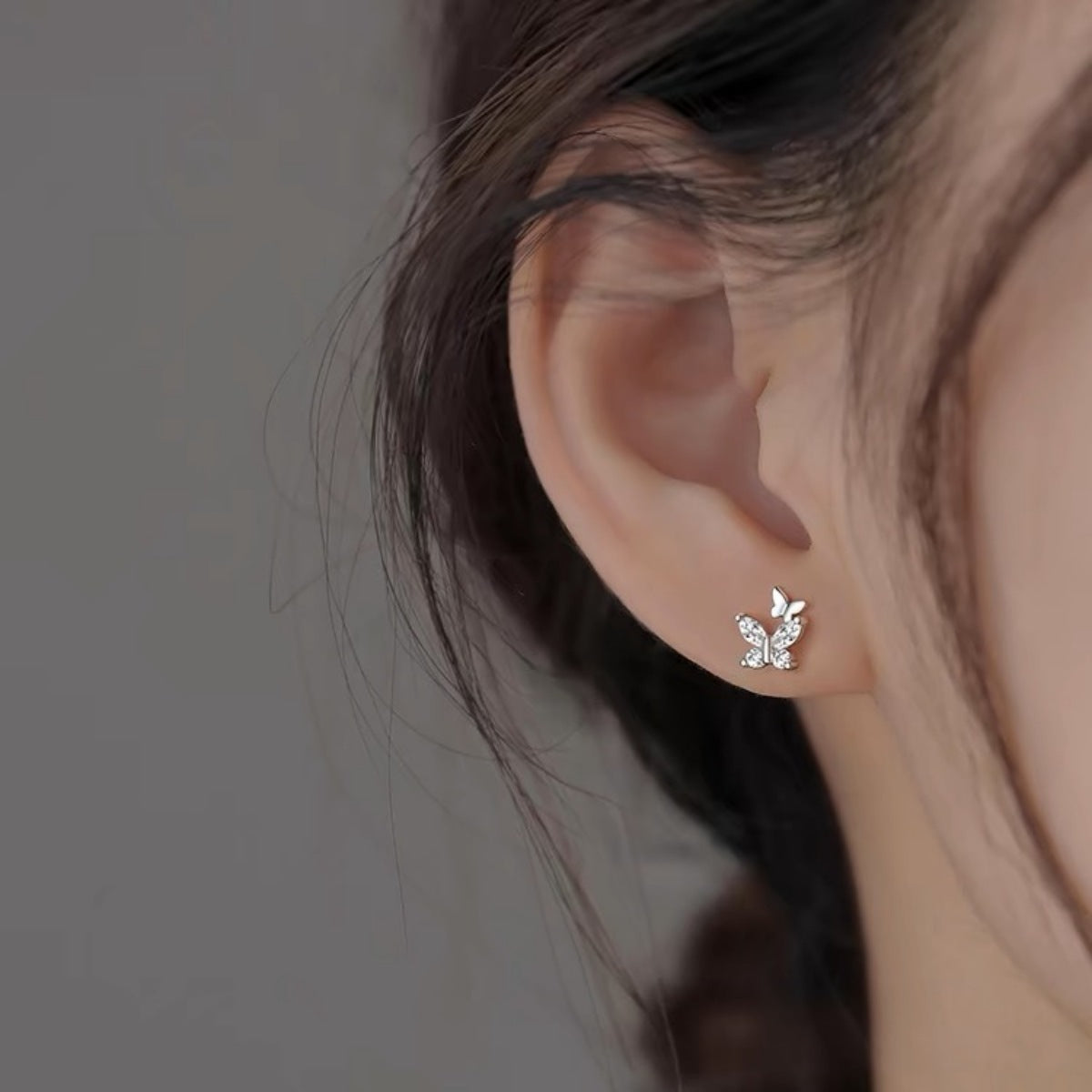 Silver-tone butterfly stud earrings with clear stones worn on a model