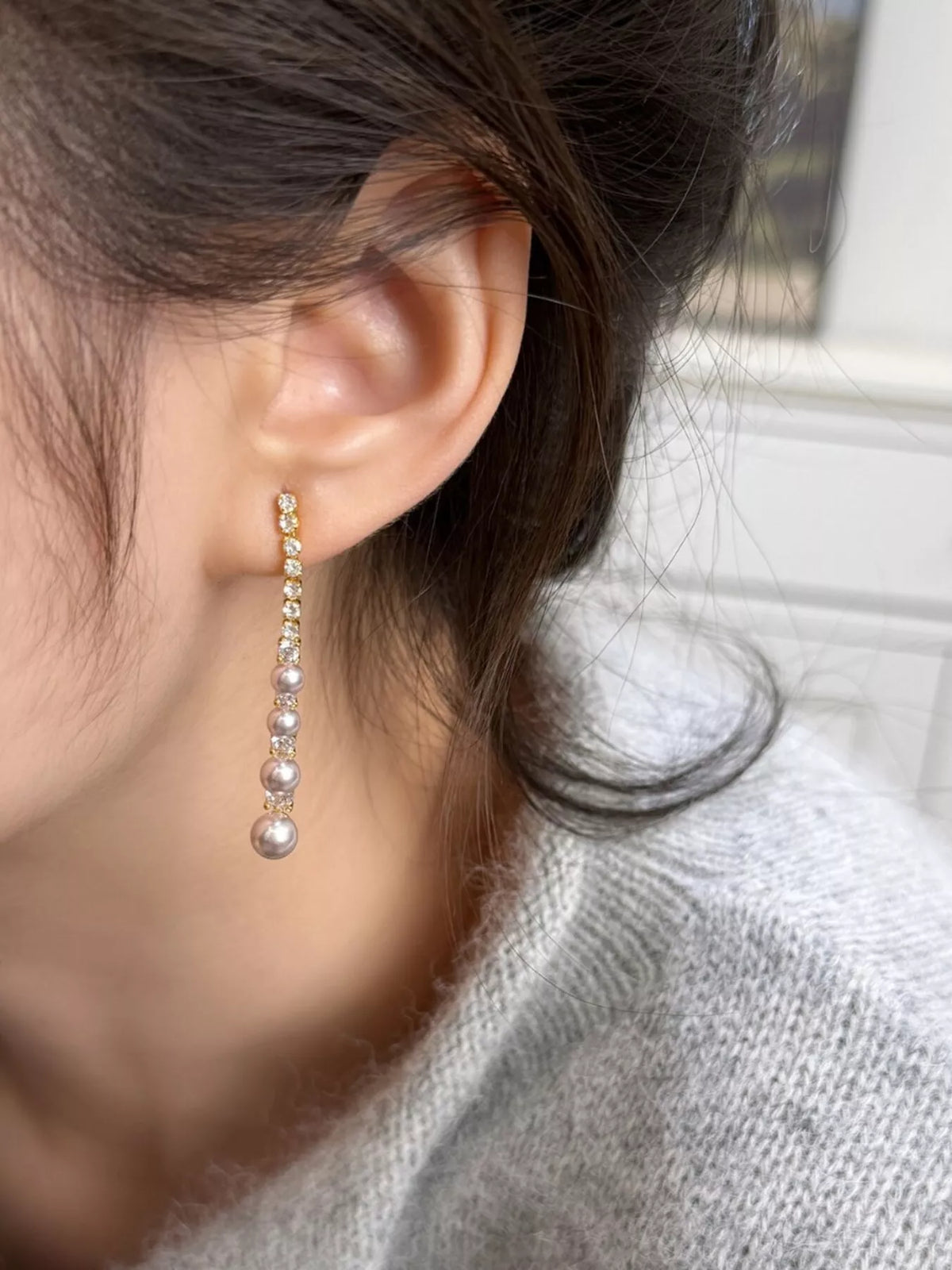 Gold-tone long pearl-like bead and clear stone drop earrings worn on a model