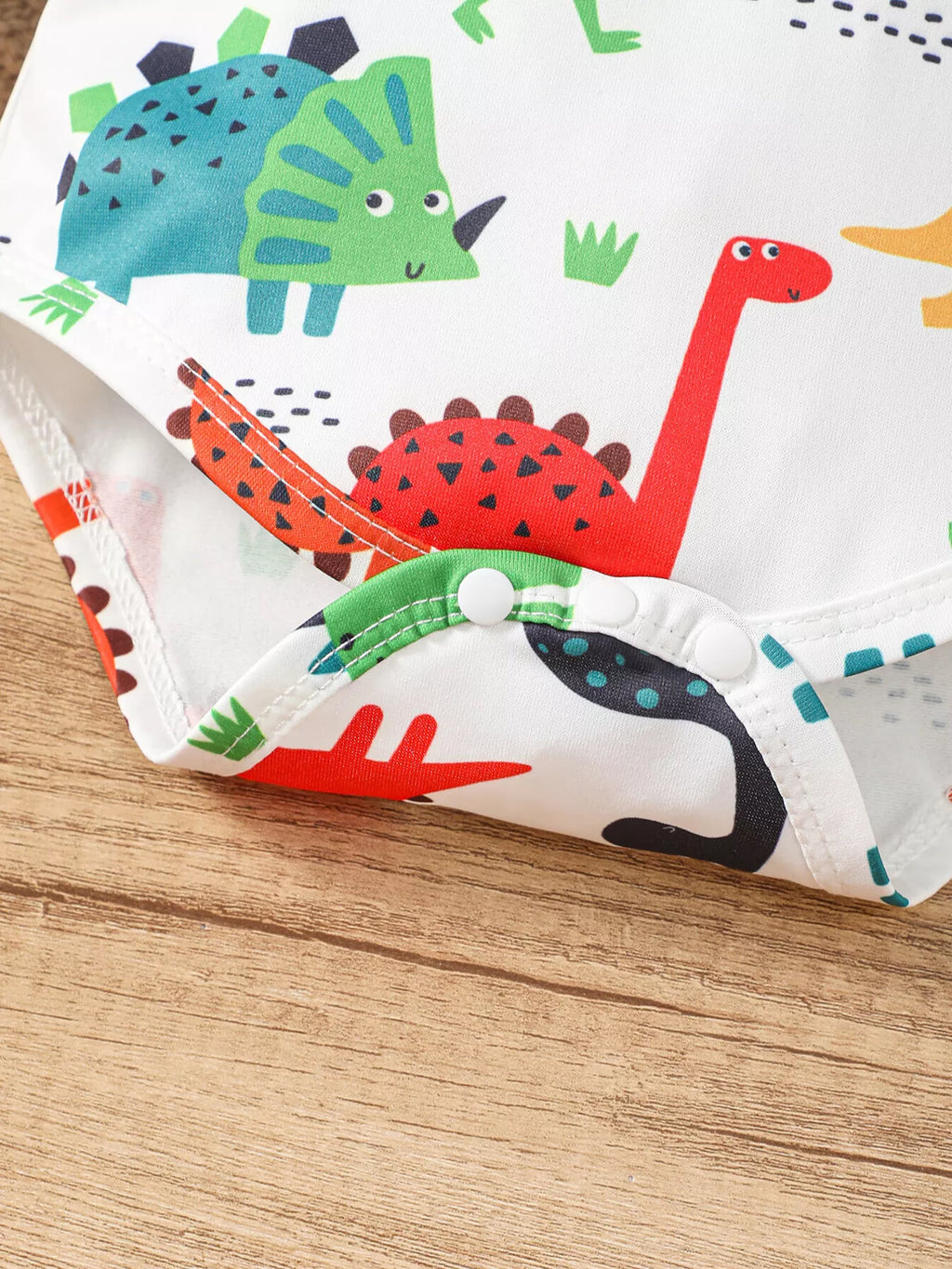 Colorful dinosaur-print fabric on the white baby bodysuit