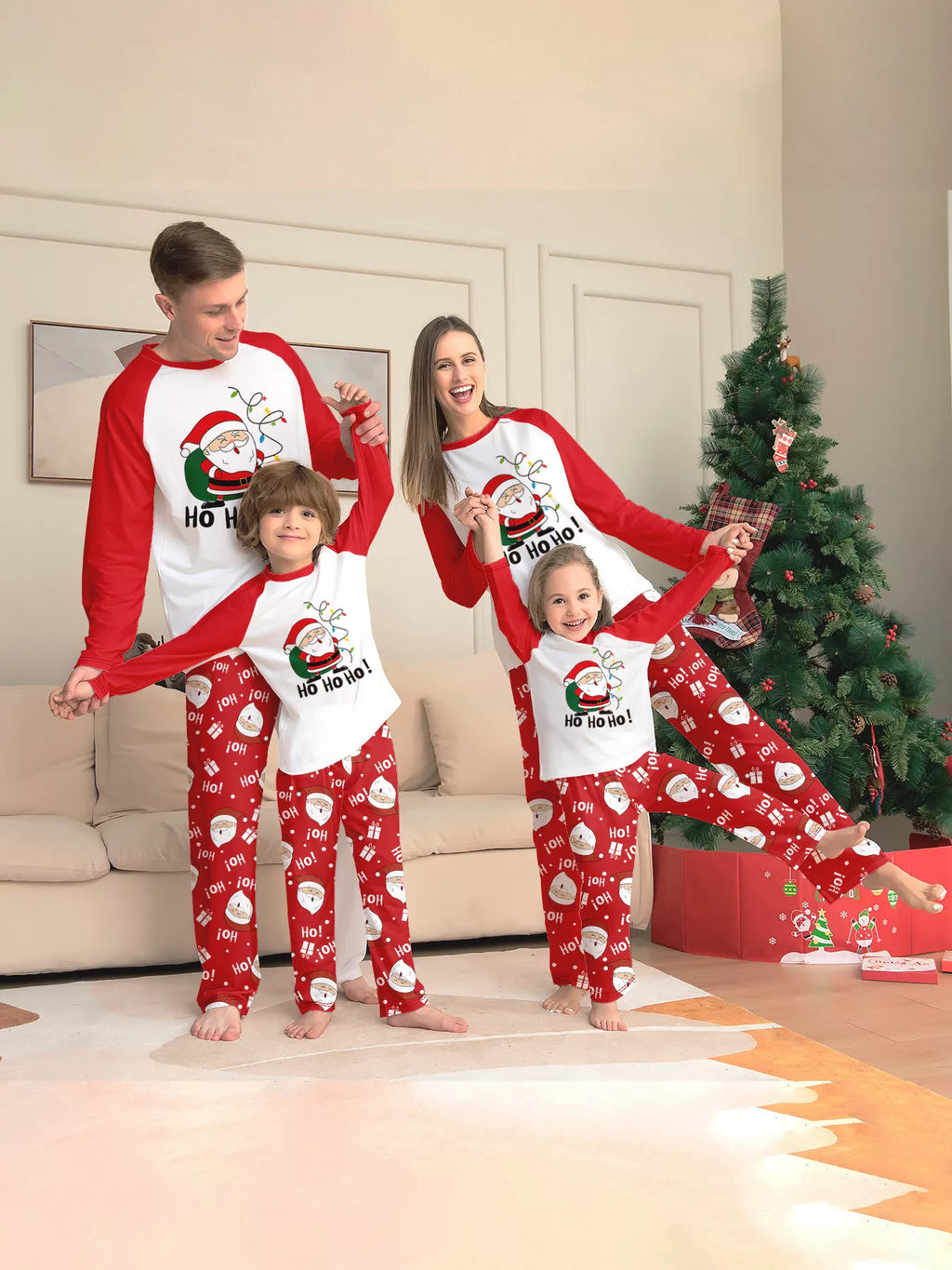 Family wearing white Santa graphic tops with red sleeves and red Santa-print pajama pants.