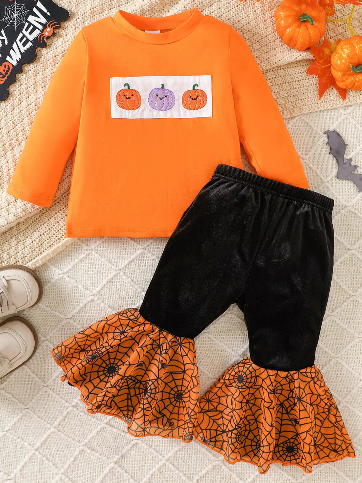 Flat lay of the orange three-pumpkin top and black flared pants with orange patterned hems.