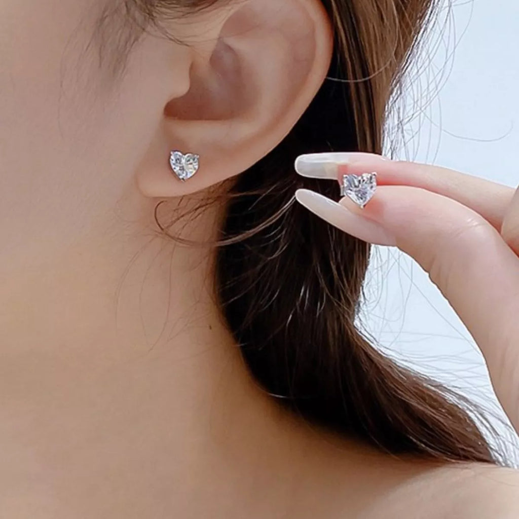 Silver-tone heart-shaped clear stone stud earrings worn on a model