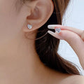 Silver-tone heart-shaped clear stone stud earrings worn on a model