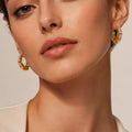 Textured gold-tone hoop earrings worn on a model