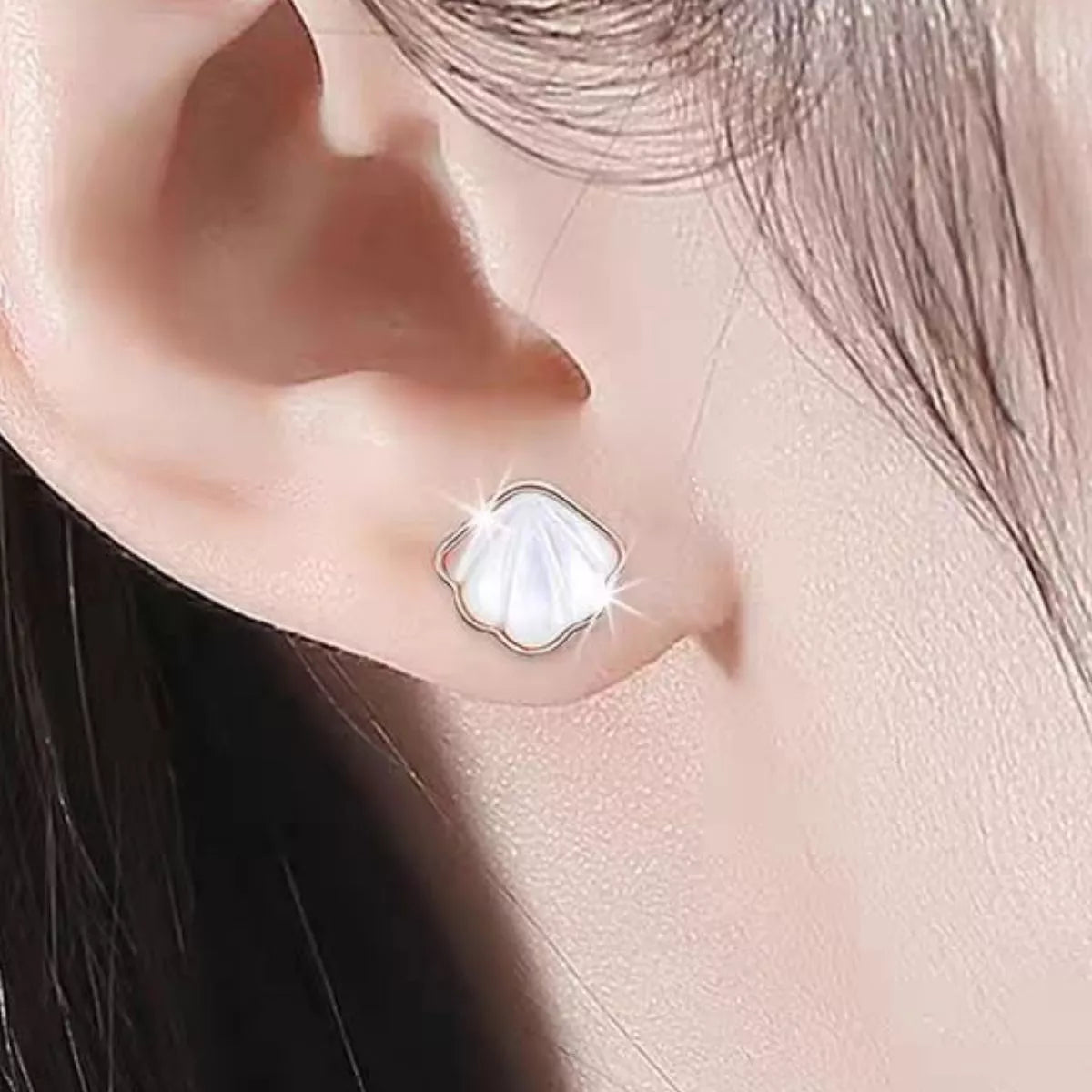 Silver-tone shell-shaped stud earrings with white centers worn on a model