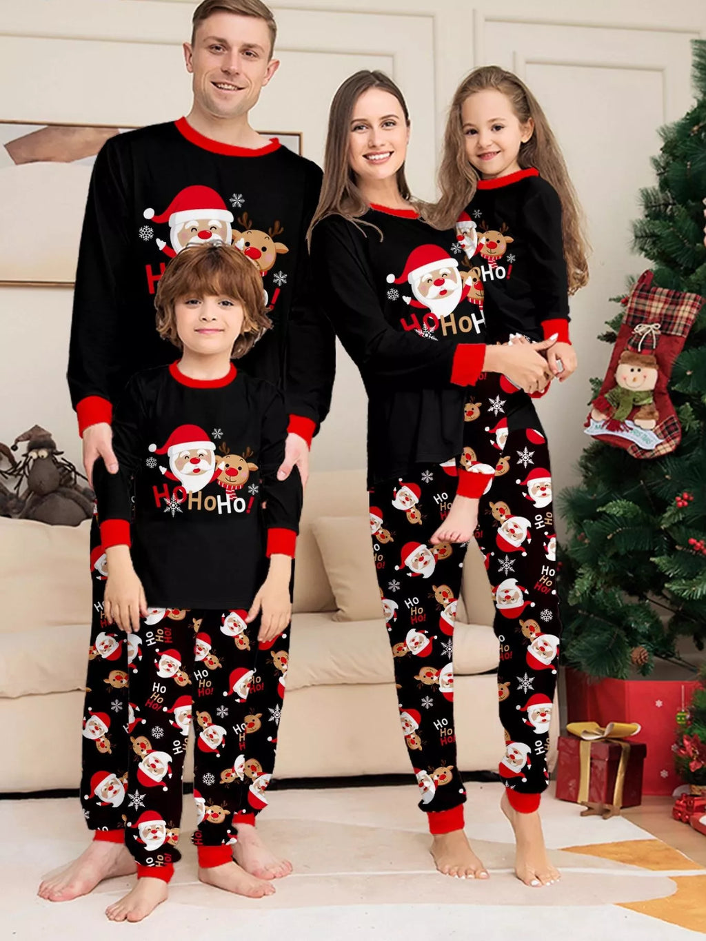 Family wearing matching black Ho Ho Ho Santa graphic tops and Santa-print pajama pants.