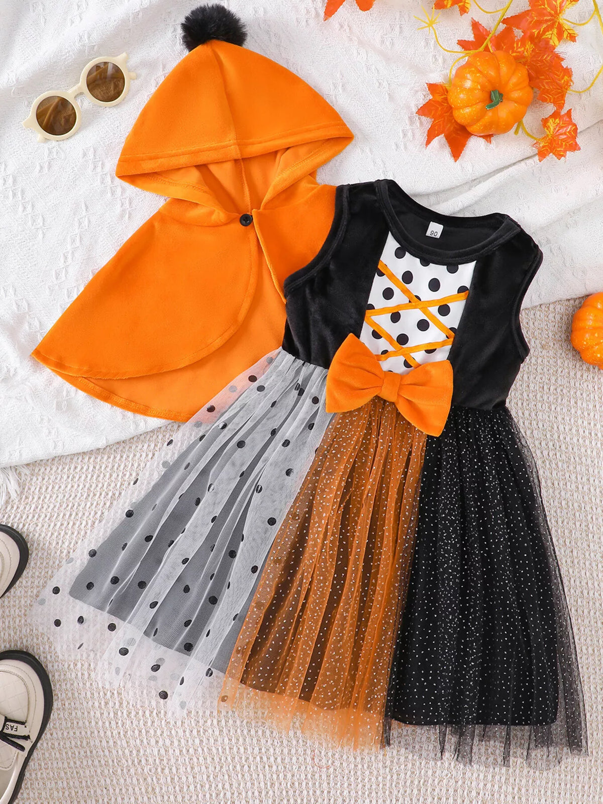 Orange hooded cape with black pom-pom paired with a black, orange and white tulle Halloween dress.