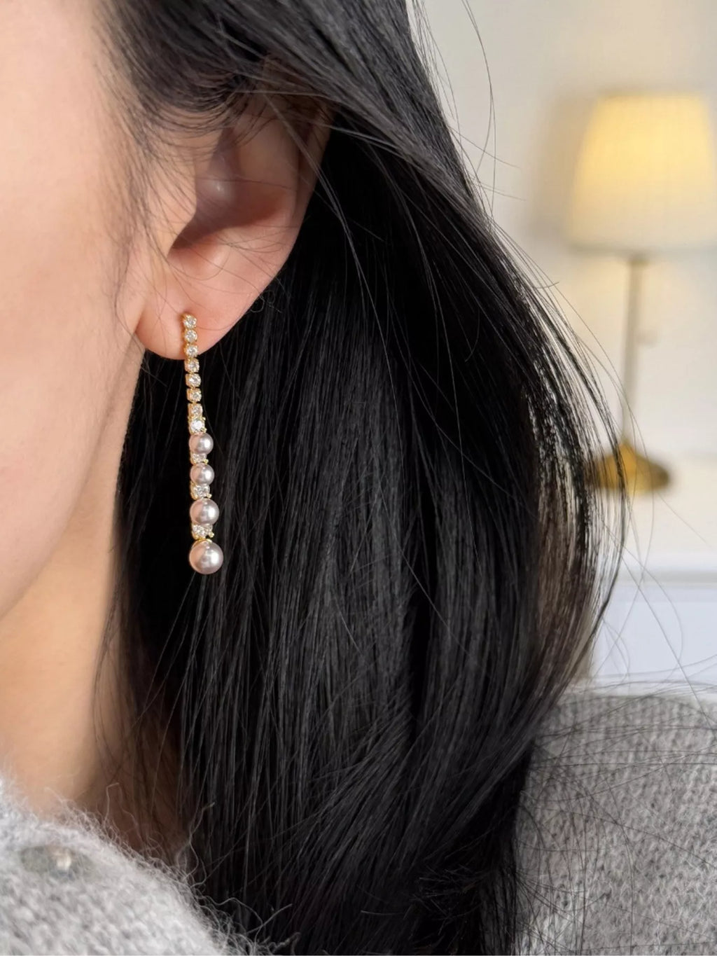Gold-tone long pearl-like bead and clear stone drop earrings worn on a model