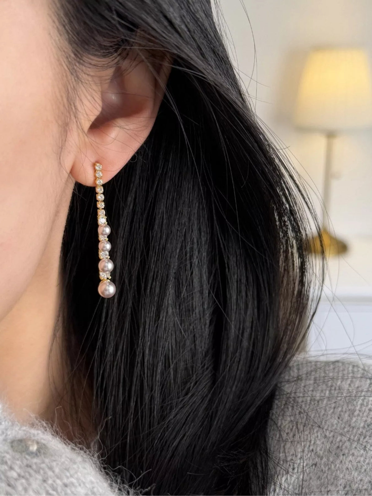 Gold-tone long pearl-like bead and clear stone drop earrings worn on a model