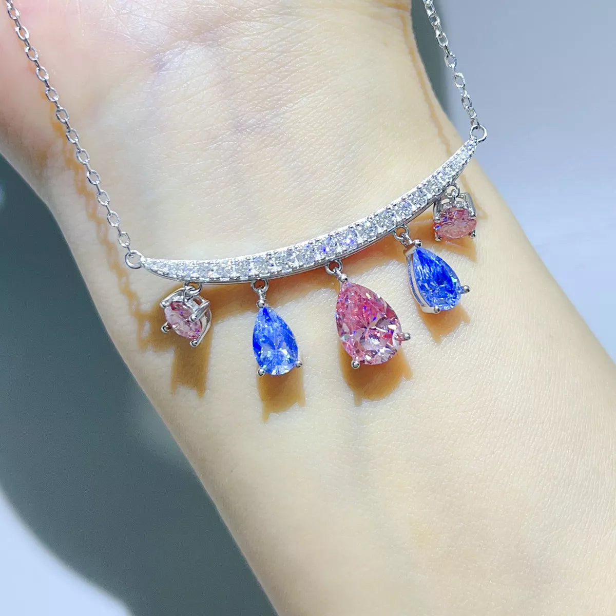 Silver-tone necklace with blue and pink teardrop stone pendants worn on a model