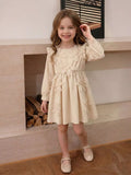Child wearing a cream long-sleeve dress with large floral appliques.