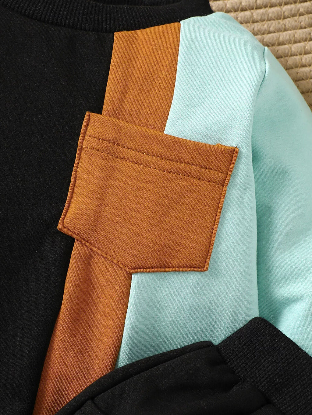 Orange patch pocket and mint panel on the black color-block sweatshirt