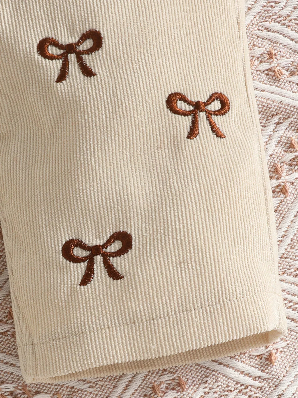 Brown embroidered bows on beige ribbed overall fabric