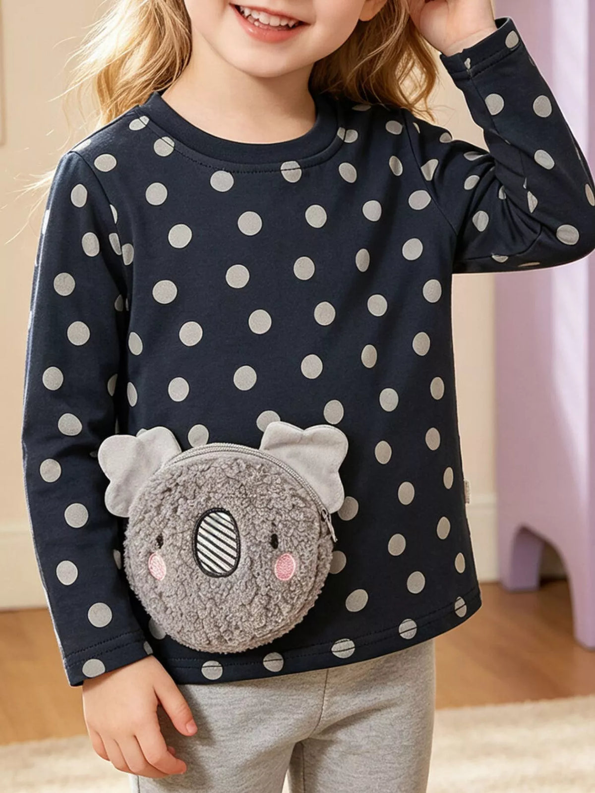 Child wearing a dark polka-dot top with a textured gray koala applique.