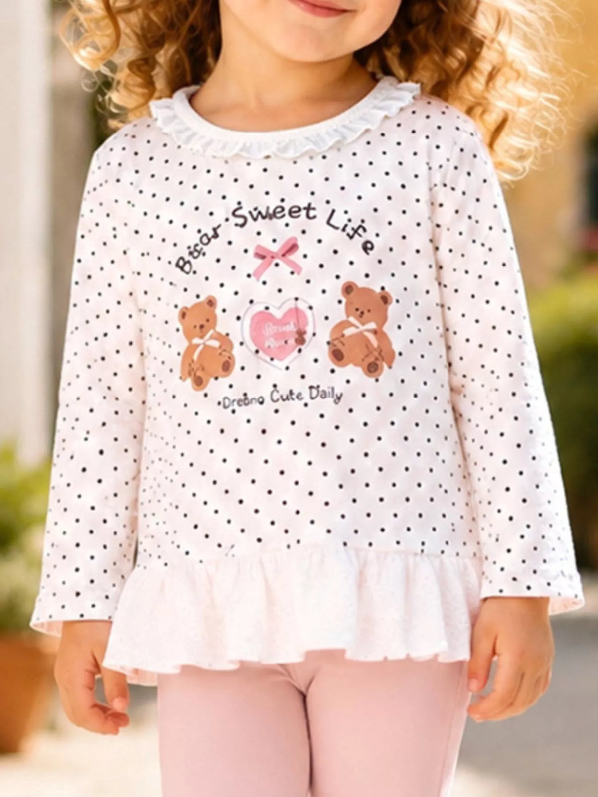 Children’s white polka-dot bear graphic ruffle-hem top with pink leggings worn by a child