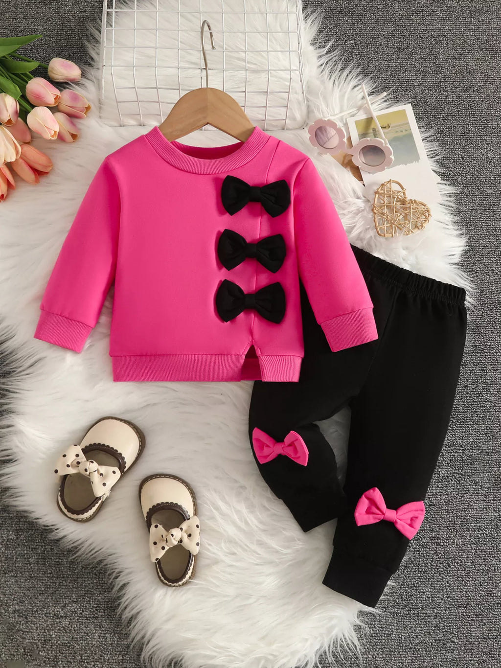 Bright pink top with black bow appliques paired with black pants and pink bows.