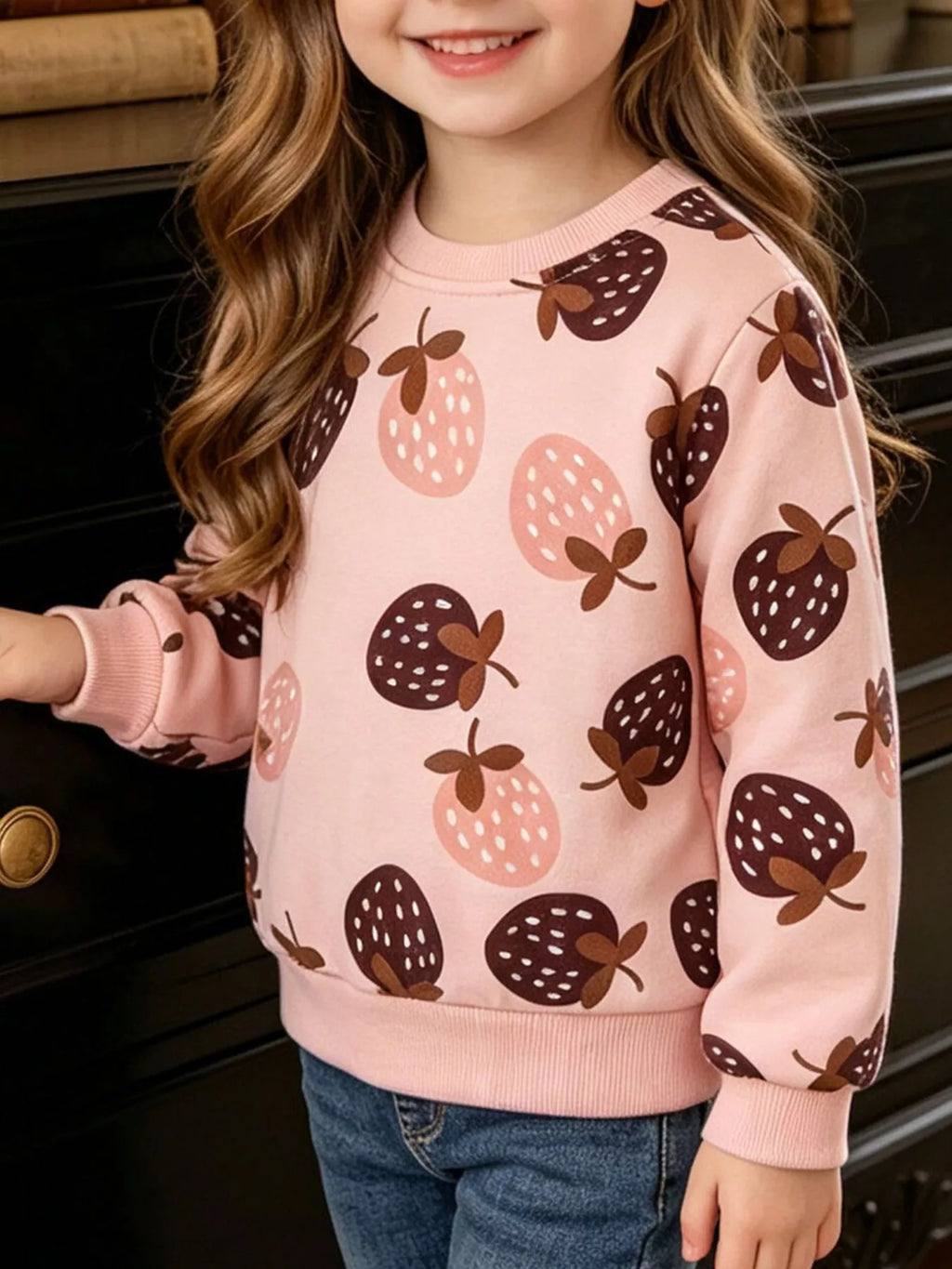 Child wearing a pink sweatshirt with dark and pale pink strawberry prints.