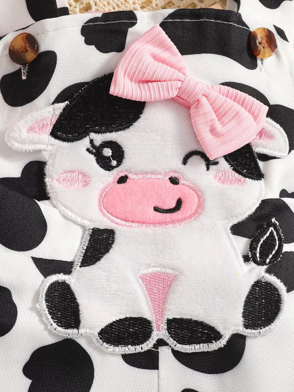 Close-up of the cow-face applique with pink bow on the cow-print overall bib.