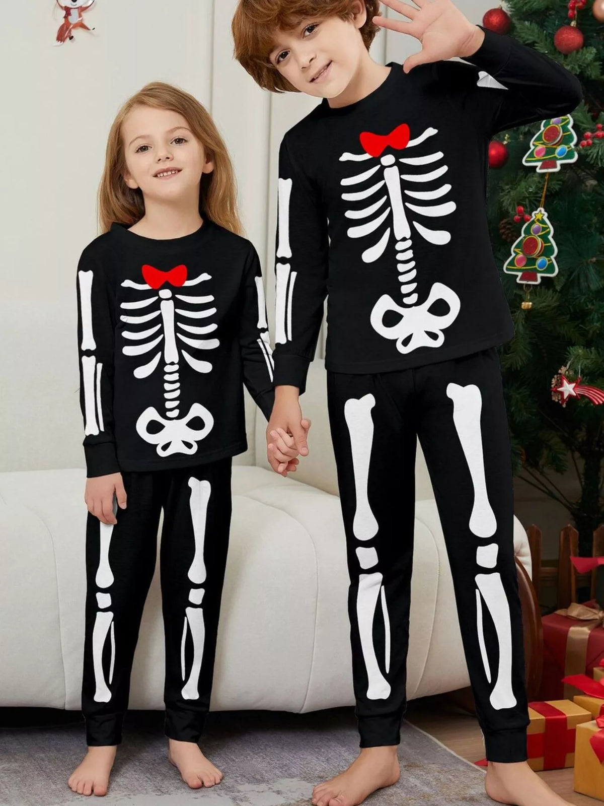 Two children wearing black skeleton-print pajamas with red bow details.