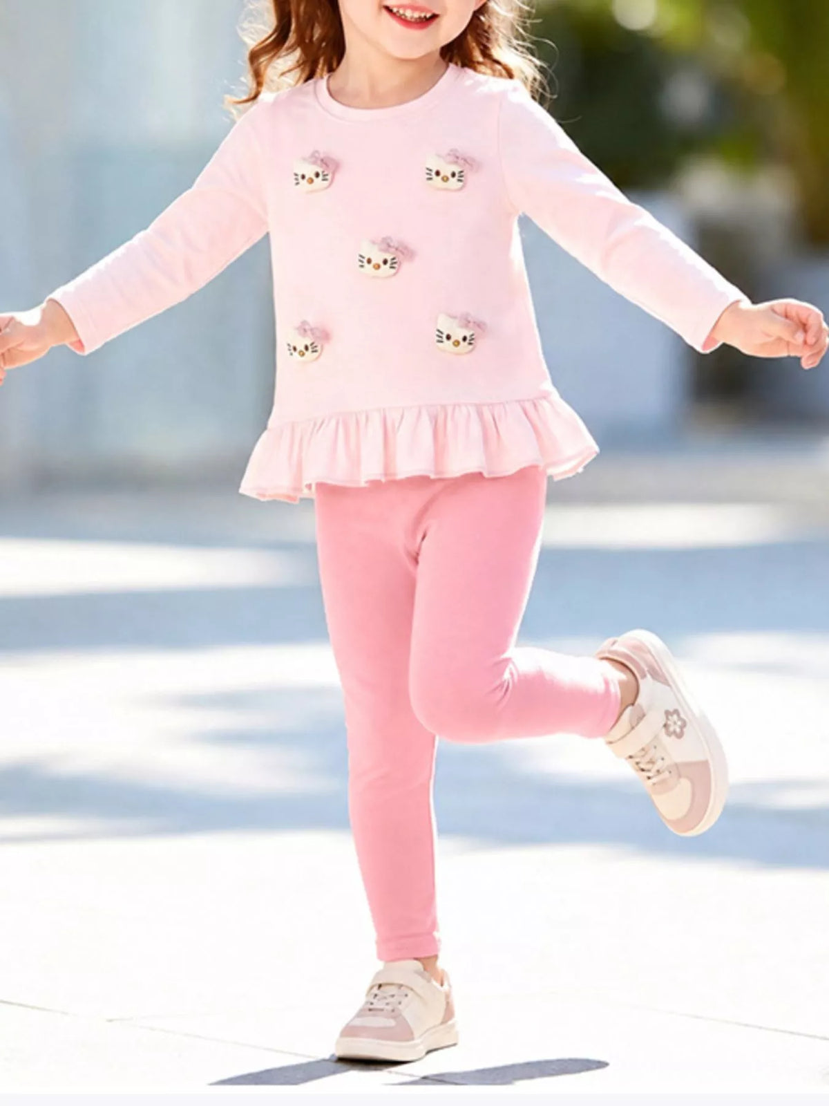 Child modeling a pink ruffle-hem top with small cat appliques and matching leggings.