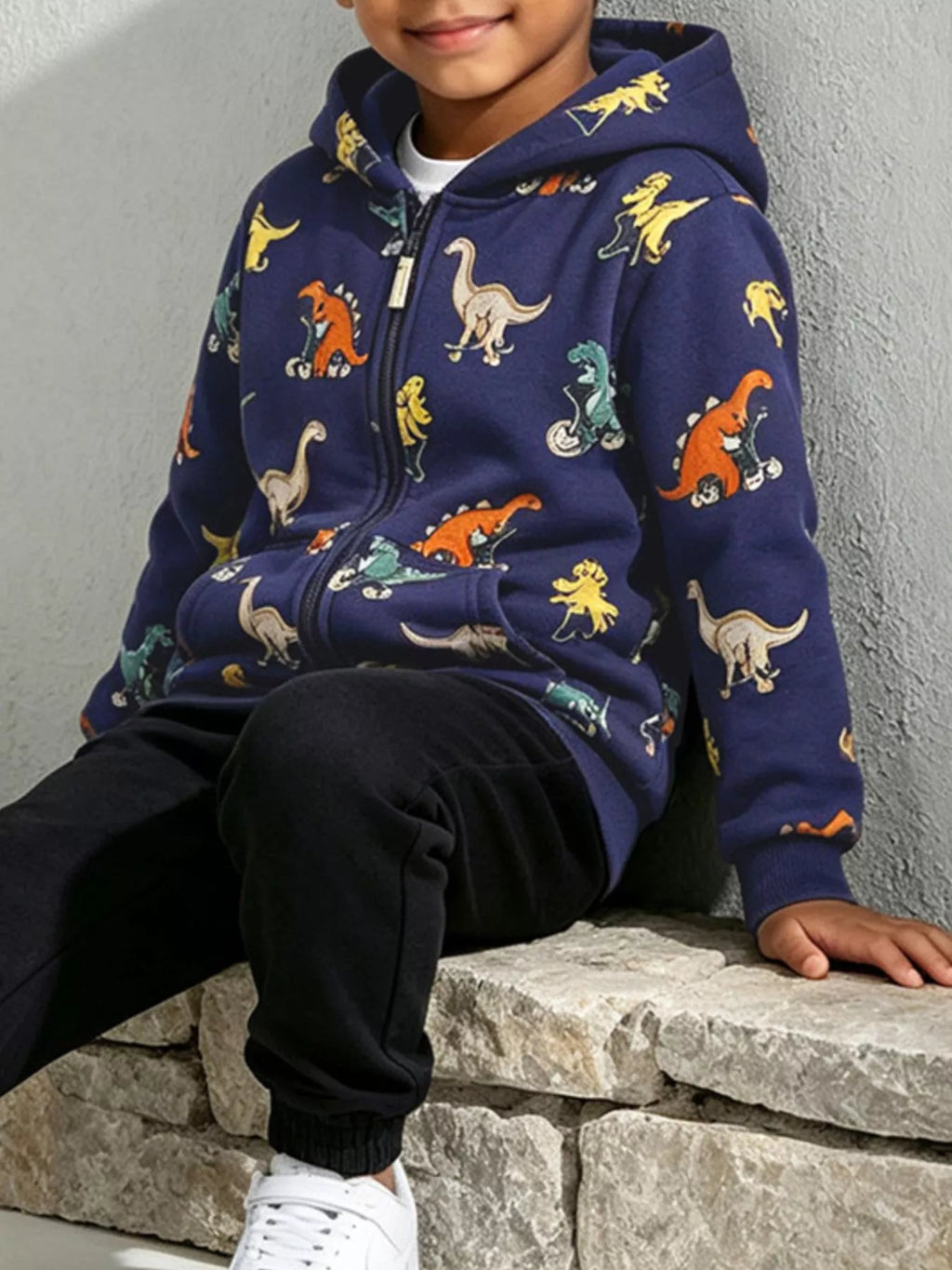 Seated child wearing a navy dinosaur-print hooded jacket.