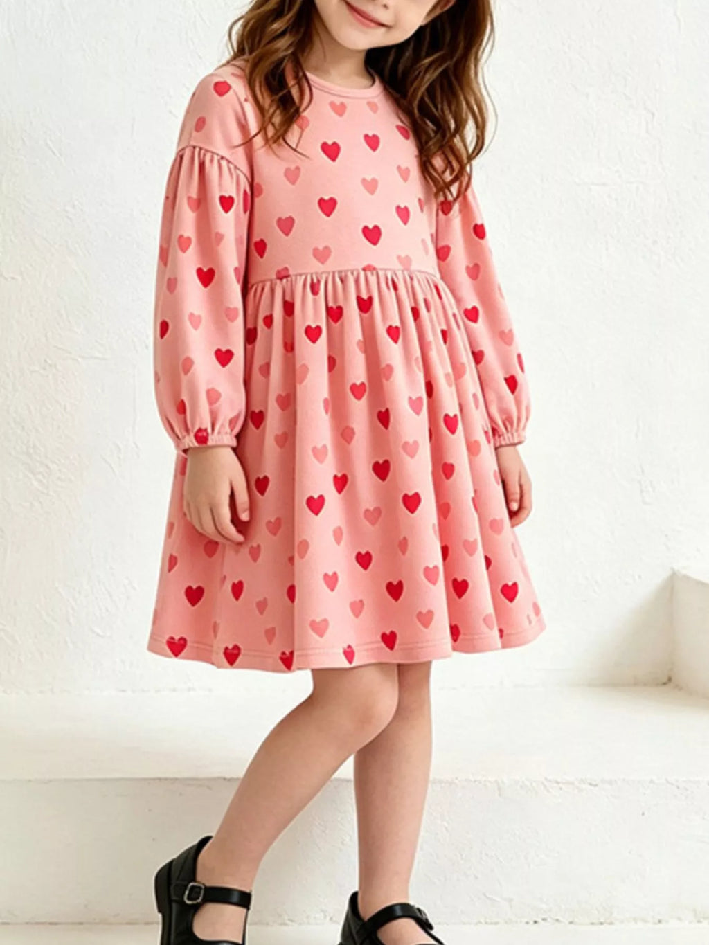 Angled view of a child modeling the pink heart-print dress.
