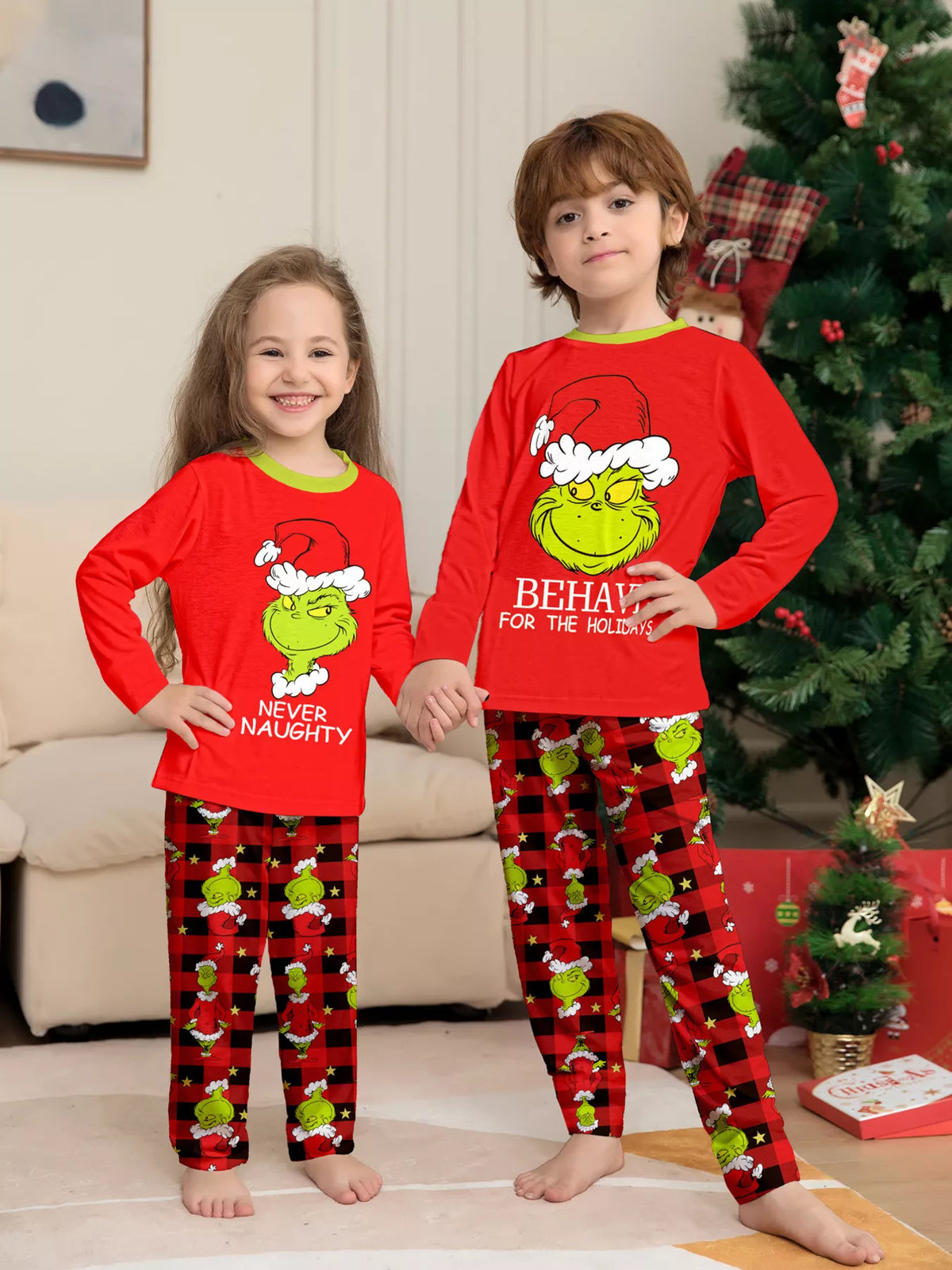 Red matching family Grinch graphic pajama top and Christmas-print pants worn by two children