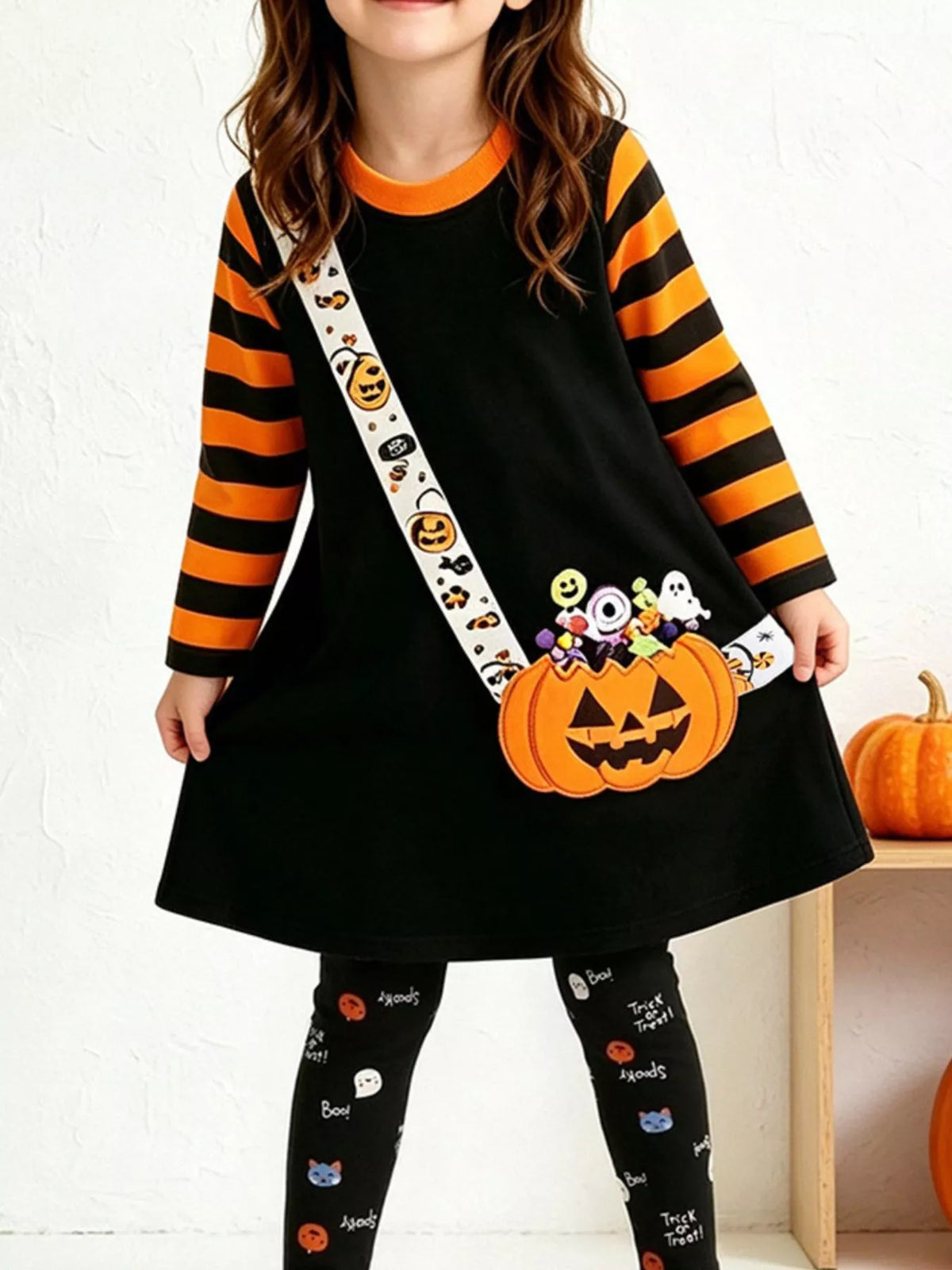 Children’s black pumpkin-print tunic with orange-striped sleeves and patterned leggings worn by a child