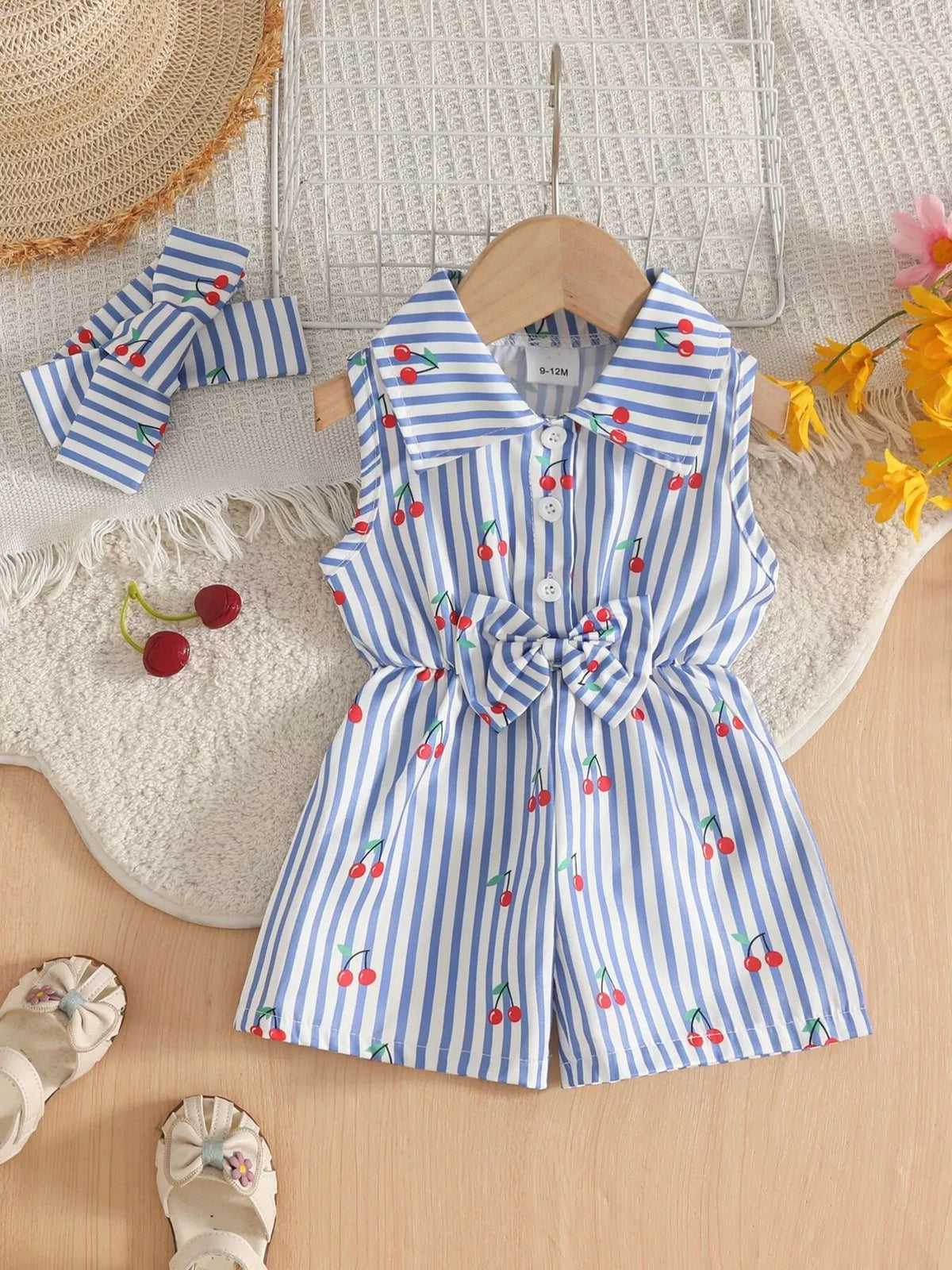 Blue-and-white striped sleeveless romper with shoulder ruffles, waist tie, cherry print and matching bow.