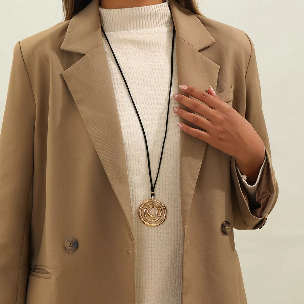 Long black cord necklace with a round gold-tone spiral pendant — detail view