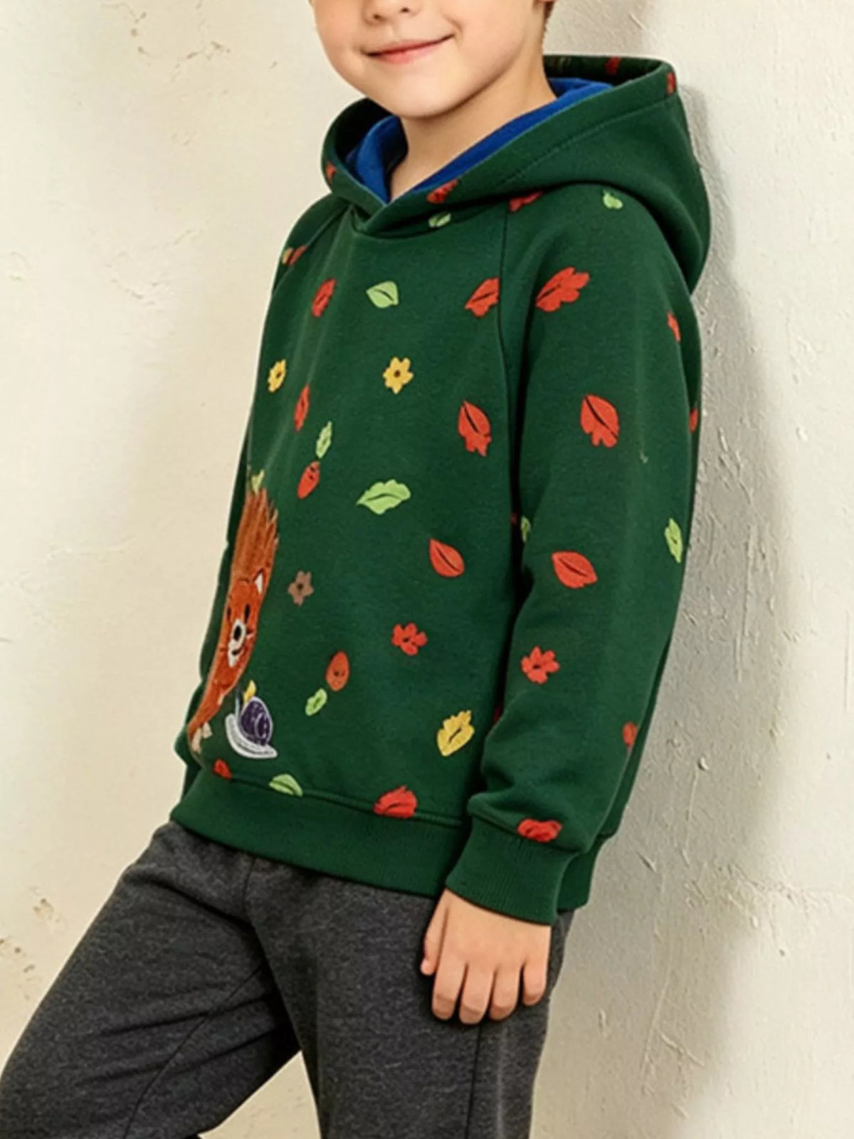 Children’s green hedgehog-print hoodie with contrasting blue hood lining worn by a child