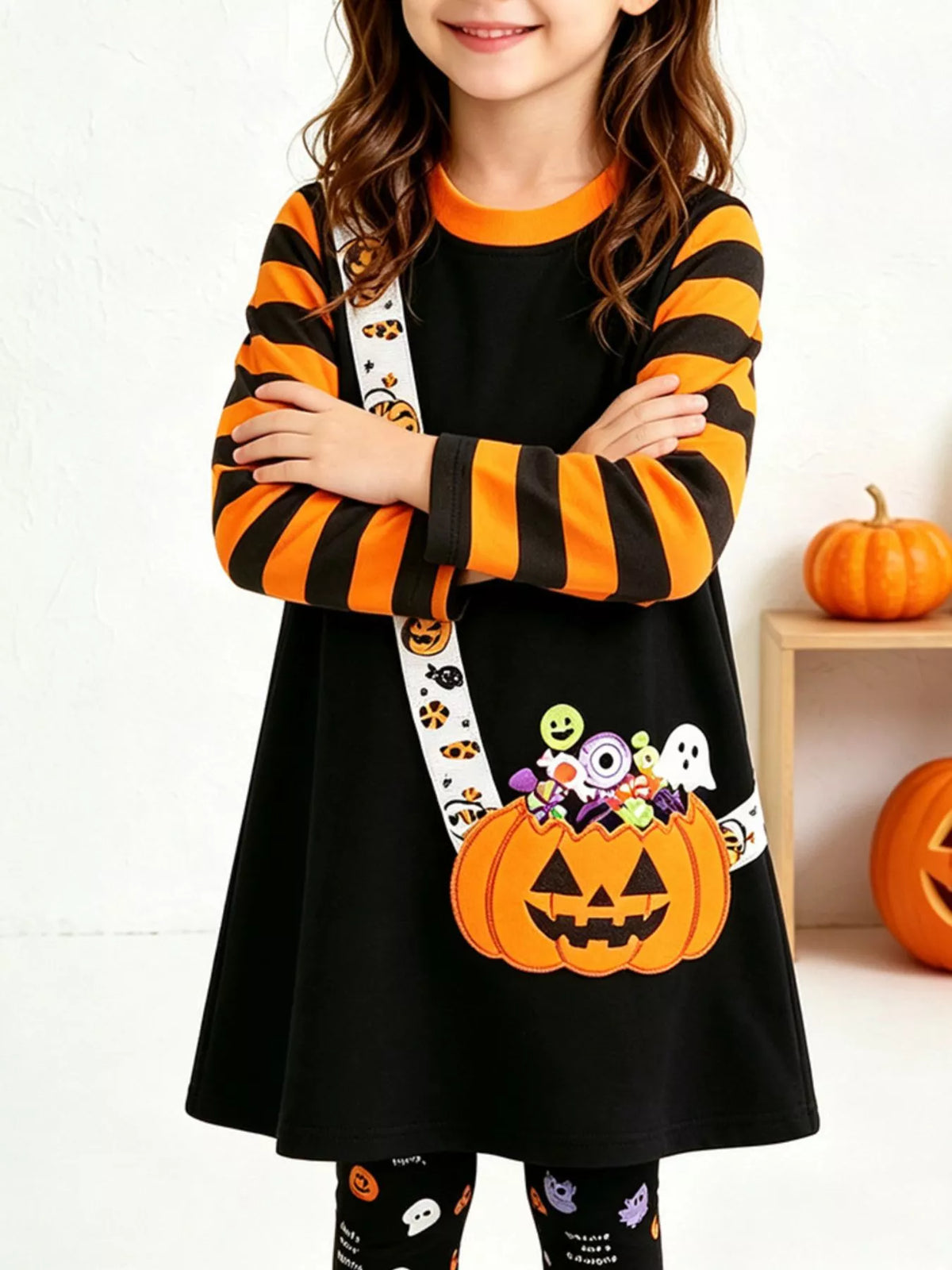 Children’s black pumpkin-print tunic with orange-striped sleeves and patterned leggings worn by a child