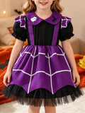 Child wearing a purple spiderweb suspender-style Halloween dress over a black puff-sleeve bodice.