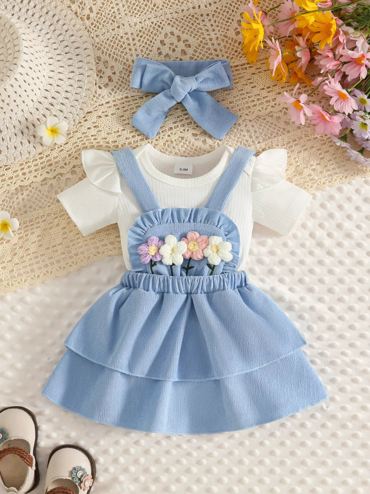 White baby bodysuit with light blue flower-applique suspender skirt and matching bow headband.