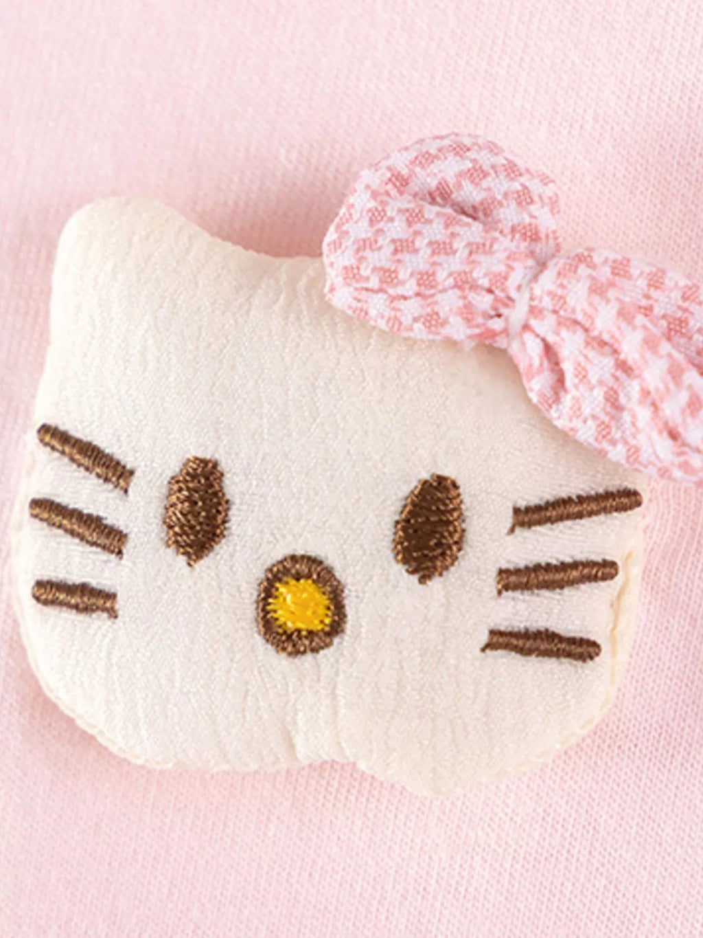 Close-up of a white cat-face applique with a pink bow on the pink top.