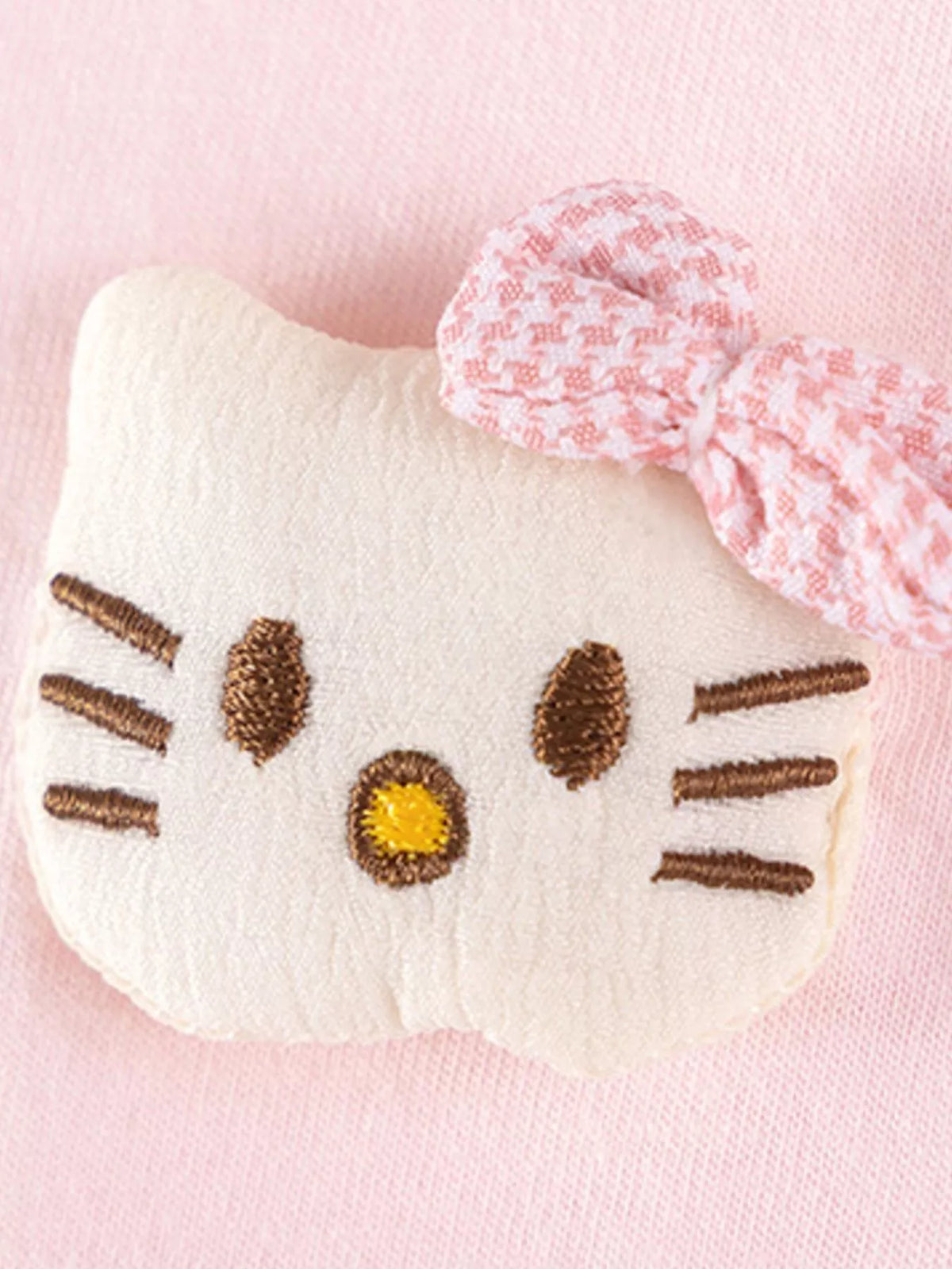 Close-up of a white cat-face applique with a pink bow on the pink top.