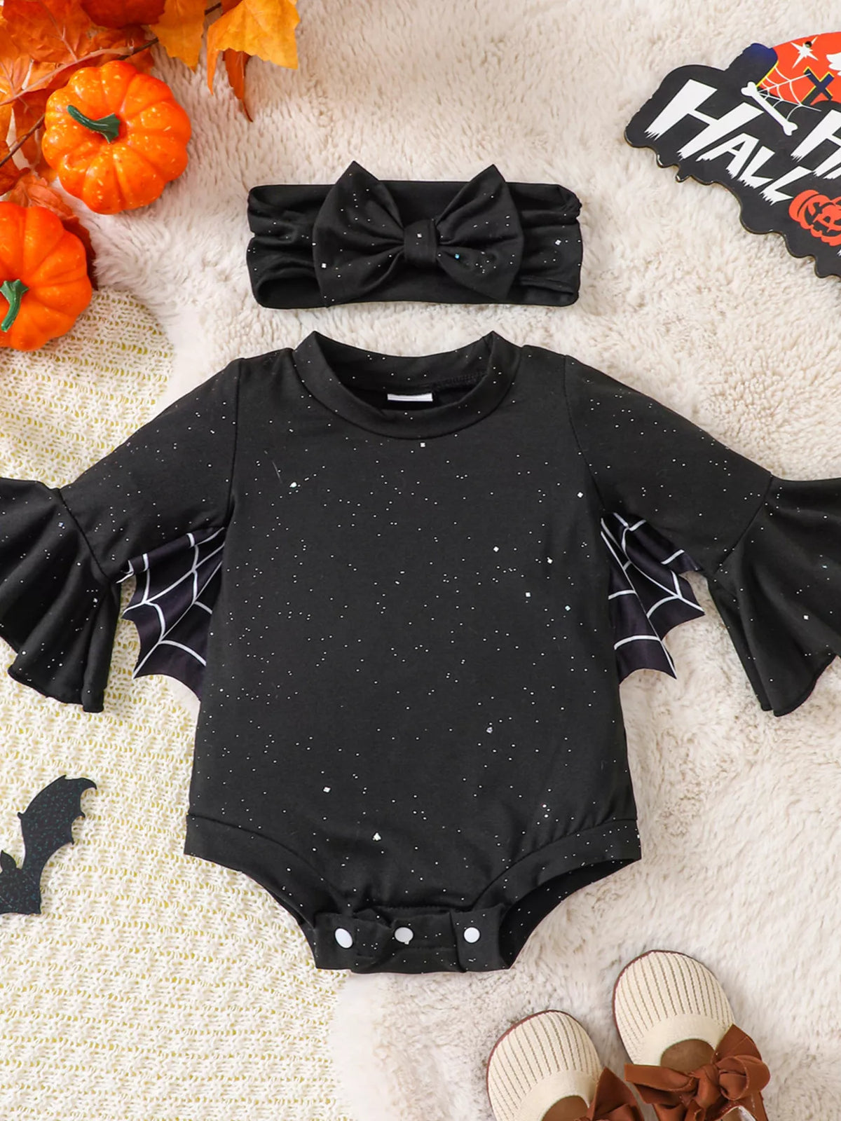 Black long-sleeve baby bodysuit with spiderweb sleeves and matching bow headband displayed flat