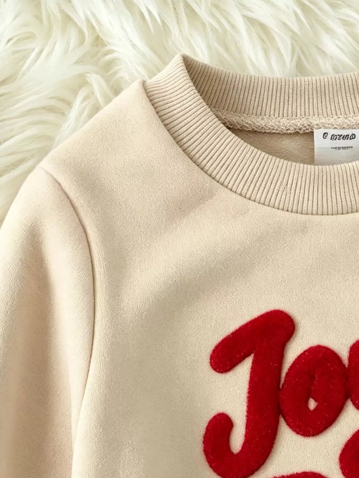 Close-up of the cream sweatshirt's ribbed neckline and red graphic.