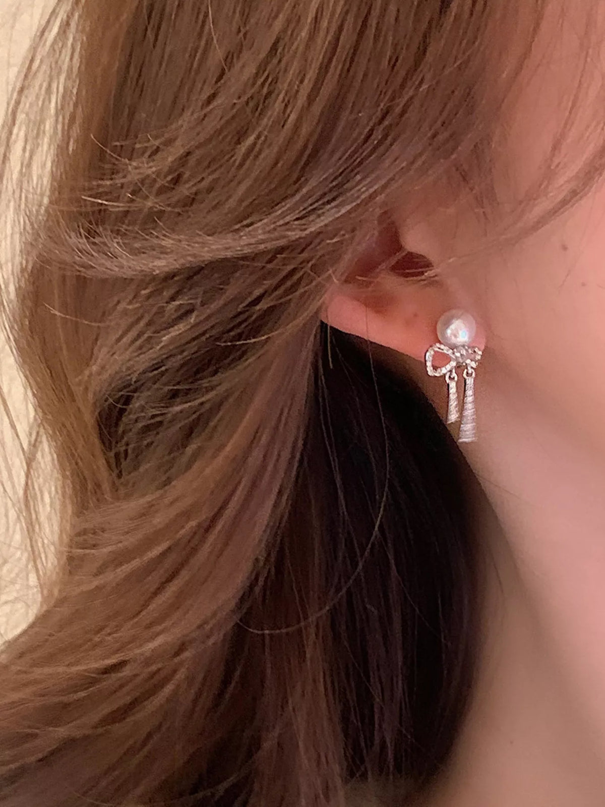 Bow-shaped drop earrings with pearl-like beads and chain tassels worn on a model
