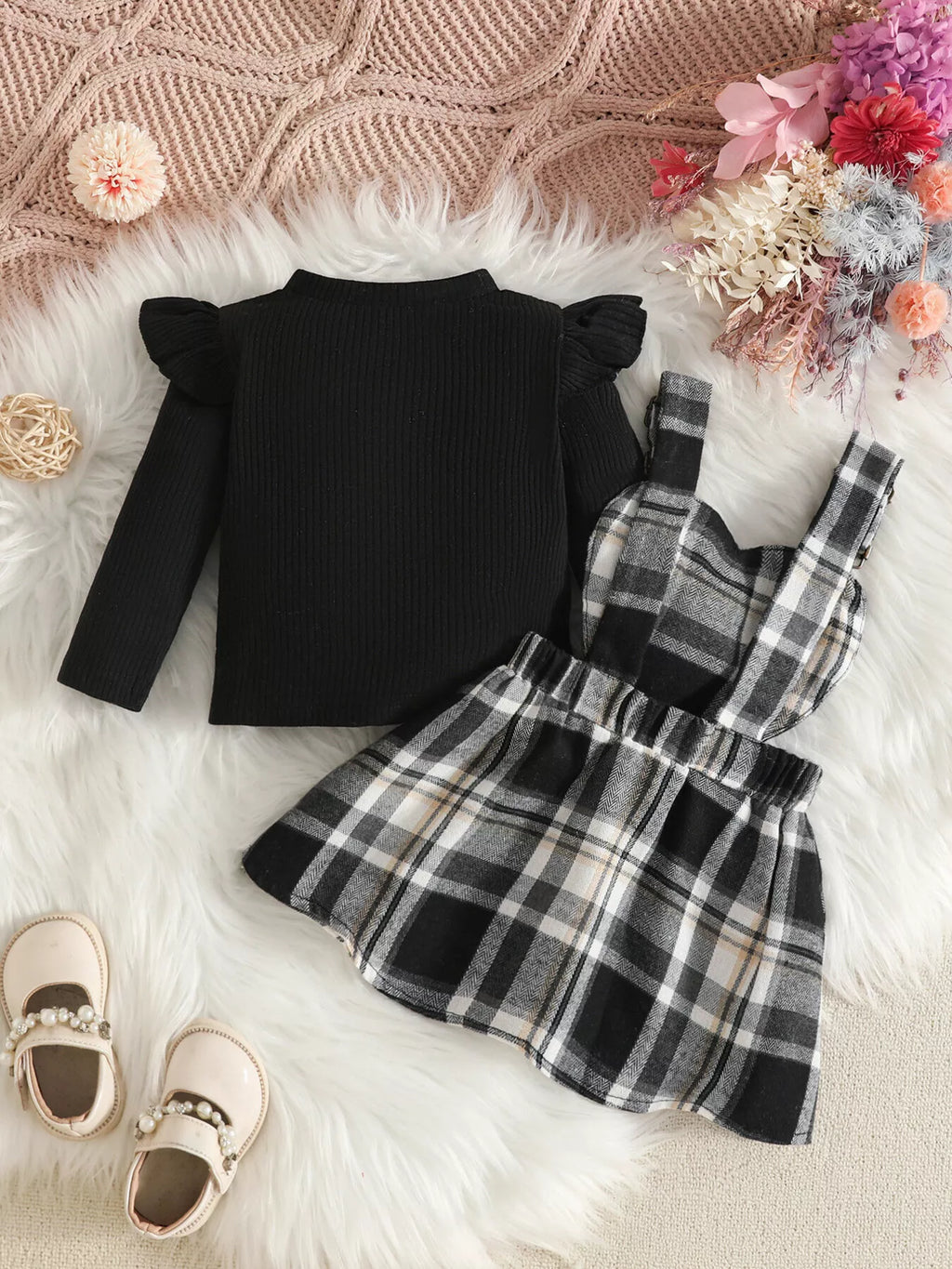 Back flat lay of the black top and black-and-white plaid suspender skirt.
