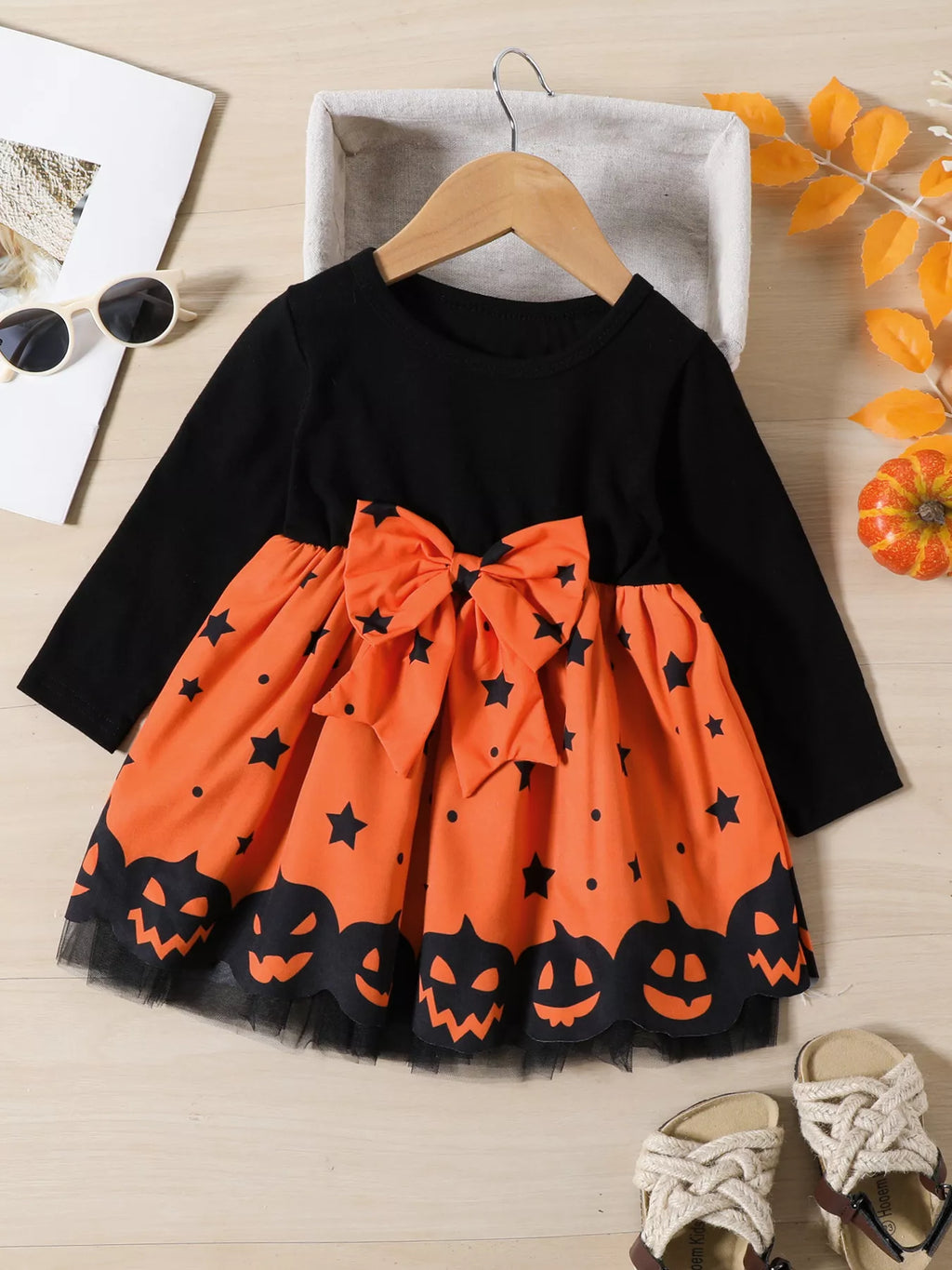 Black long-sleeve dress with orange pumpkin-print skirt and waist bow displayed flat