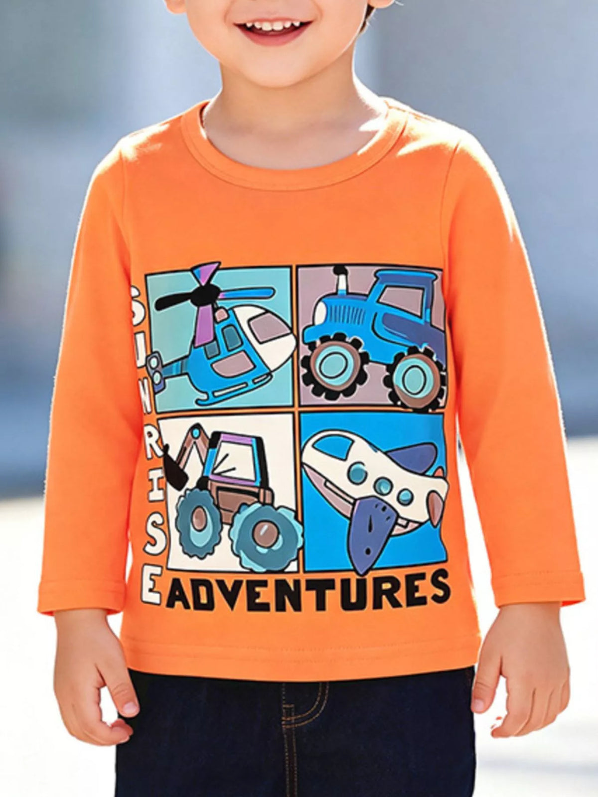 Child wearing an orange long-sleeve vehicle graphic shirt.