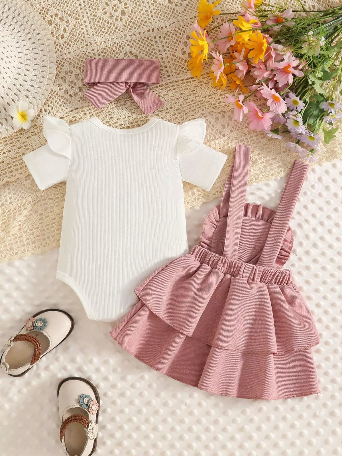 Back flat lay of the white bodysuit, dusty pink suspender skirt and headband.